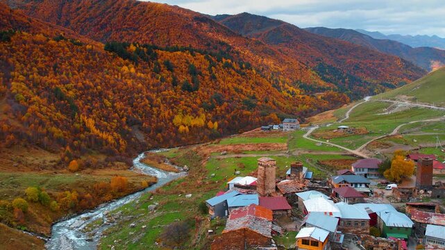 Footage over picturesque old village Ushguli with medieval tower houses. Thin narrow river flows at the mountains foot. Orange woods cover the rocks. Autumn in Upper Svaneti, Georgia.