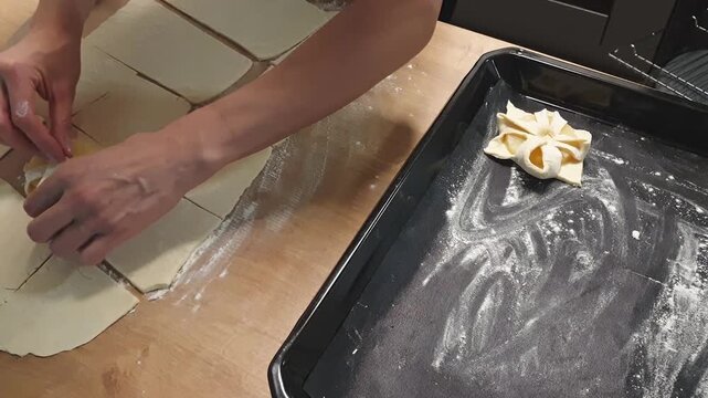 A woman wraps a pineapple wedge in puff pastry and places it on baking tray. Food
