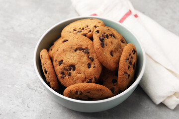 Delicious chocolate chip cookies in bowl on gray textured table, closeup