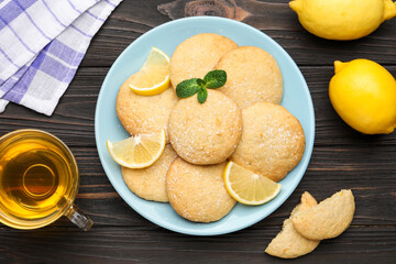 Tasty lemon cookies and fruit slices on black wooden table, flat lay