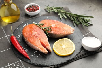 Pieces of salmon fillet with spices, lemon and oil on gray table, closeup