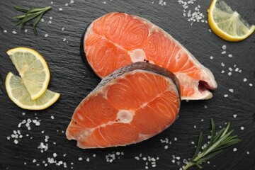 Pieces of salmon fillet with spices and lemon on black textured table, flat lay