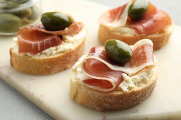 Delicious bruschettas with cream cheese, prosciutto and green olives on table, closeup