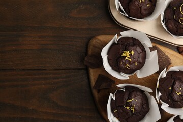 Tasty chocolate muffins with lemon zest on wooden table, flat lay. Space for text