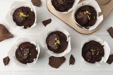 Naklejka premium Tasty chocolate muffins with lemon zest on white tiled table, flat lay