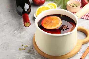 Tasty mulled wine in pot and ingredients on gray textured table, closeup