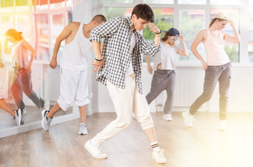 Fototapeta premium Positive young man engaged in hip-hop together with other attendees of dancing courses