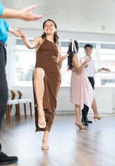 Fototapeta premium Motivated smiling young girl in bodycon brown dress dancing vigorous lindy hop with partner at group dance rehearsal in modern choreography studio..