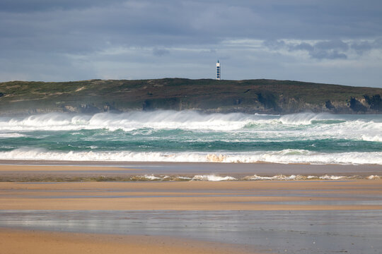 Wild crashing waves on beach with lighthouse ferrol
