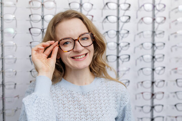 Happy woman adjusting eyeglasses in optometry store choosing new eyewear
