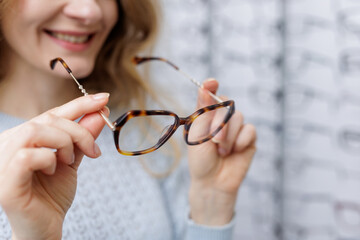 Close up woman holding tortoiseshell eyeglass frame in optical store choosing eyewear