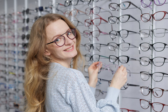 Smiling woman selecting eyeglass frames in optical store eyewear shopping and vision care
