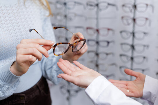 Hands passing eyeglass frames during optician consultation in optical store eyewear selection
