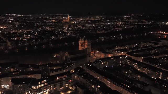 Drohnenvideo ueber St. Maximilian im Glockenbachviertel mit hellen Strassen, reflektierender Isar, historischer Architektur und deutlicher Nachtstimmung des zentralen Stadtteils.