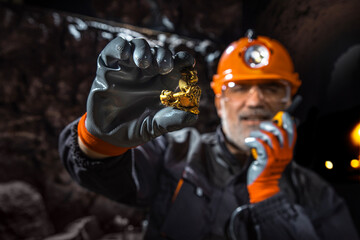 Man in a hard hat with a flashlight holding gold nugget, reporting a discovery by walkie-talkie. Gold vein. Geology, speleology, mining with a scientific approach