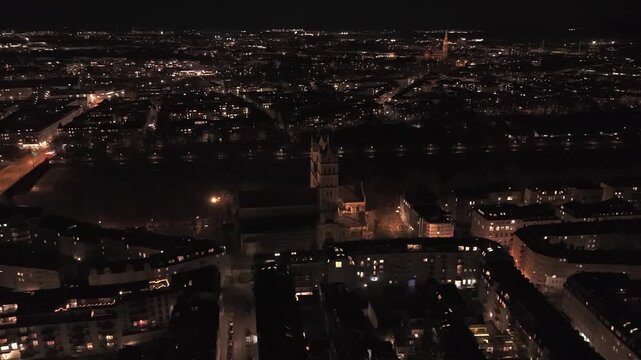 Droneperspektive auf St. Maximilian in der Isarvorstadt, mit beleuchteten Strassen, Flussnaehe, urbanem Muster und der eindrucksvollen Kirche als dominantes Element der Nachtszenerie.