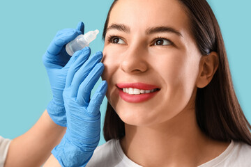Doctor's hands with eye drops and woman on blue background, closeup