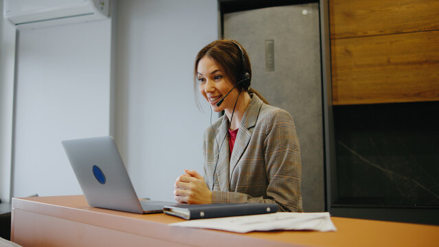 Woman at a desk using a laptop and headset while talking to a client in an office setting during daytime