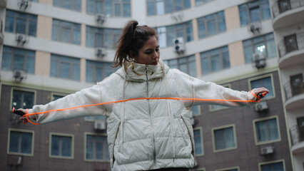 Woman in a light jacket prepares her jump rope in an urban courtyard surrounded by tall apartment...