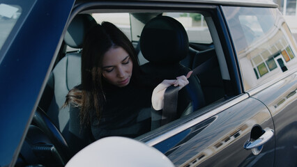 Woman teaching safety by buckling seatbelt in car before driving in urban area near shops during...