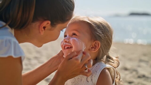 Mother applying sunscreen to her daughter's face, ensuring protection. The little girl is smiling and enjoying the moment with her mother on beach Stock Video