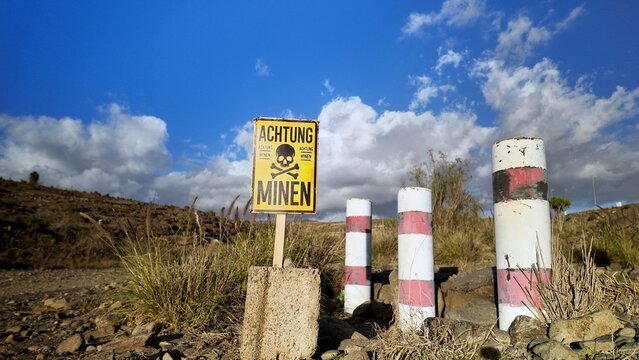 Yellow warning sign Achtung Minen with a skull and crossbones symbol standing in a dry, desolate landscape, indicating a dangerous area with potential landmines