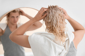 Naklejka premium Young blonde man washing hair near mirror in bathroom, back view