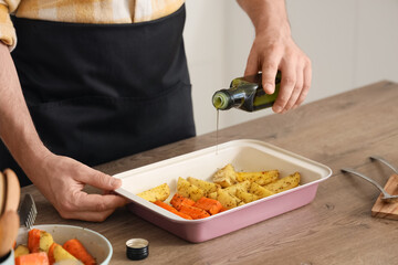 Young man cooking vegetables in baking dish at home