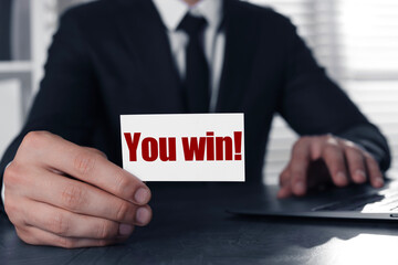 Obraz premium Businessman holding card with phrase You Win! at table in office, closeup