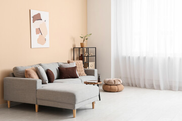 Interior of light living room with grey sofa, poufs and big window