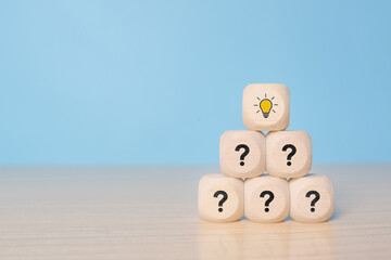 Pyramid of wooden blocks or cubes with question mark symbol icons stacked on wooden table with light bulb symbol on top, faq, question and answer or support concept