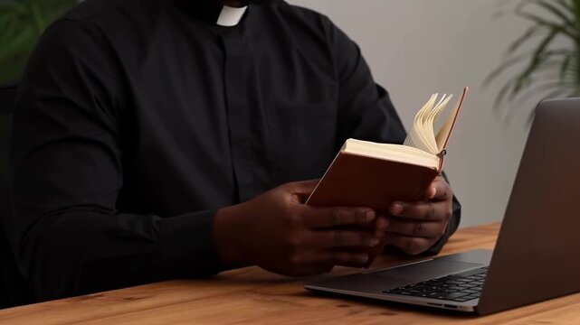 A clergyman reads a book with laptop. It depicts a person dressed in a clerical collar reading a book at a desk Stock Video