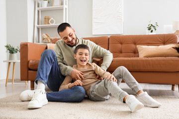 Happy father having fun with his son on floor near brown leather sofa at home