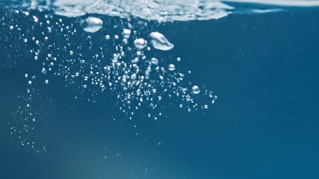 Closeup of clear water with numerous small and large air bubbles rising from the bottom to the surface against a blue background.