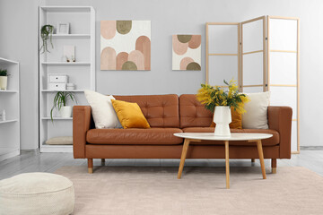 Interior of light living room with sofa, shelf unit and mimosa flowers in vase on table
