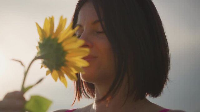Sunflower field serenity, Silent smile amidst sunflower field at sunset capturing peaceful connection, Calm female figure with short hair peacefully smelling sunflower during warm sunset light