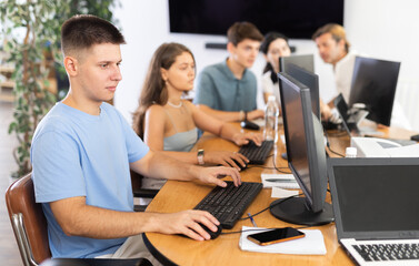 Fototapeta premium Engrossed in his work, student sits near computer, fully immersed in his studies.