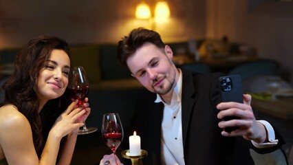Happy young man holding smartphone while making selfie with her girlfriend during date in the...