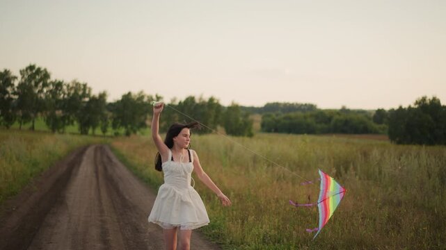 Joyful countryside running, Girl joyfully runs through fields, Youthful girl with colorful kite in rural setting, Cheerful girl in flowing dress sprints across grassy meadow with bright kite