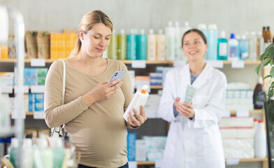 Fototapeta premium Pregnant woman scanning qr code for cream with woman pharmacist in pharmacy