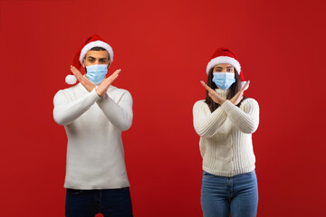 A young arab couple stands against a red background wearing masks and Santa hats.