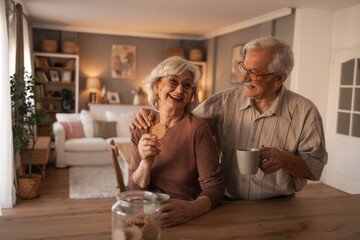 Warm Home Scene: Happy Senior Couple Sharing Cookies and Coffee at the Cozy Kitchen Counter