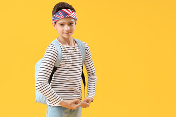 Portrait of fashionable schoolboy with backpack flexing on orange background