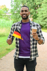 Fototapeta premium Young man with flag of Germany and coffee cup in park