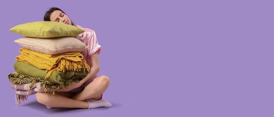 Beautiful young woman with stack of different blankets and pillows sitting on purple background