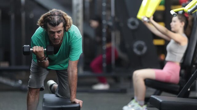 Adult man does back exercises with dumbbells in the gym, he works hard to develop muscle strength and build an athletic figure. High quality 4k footage