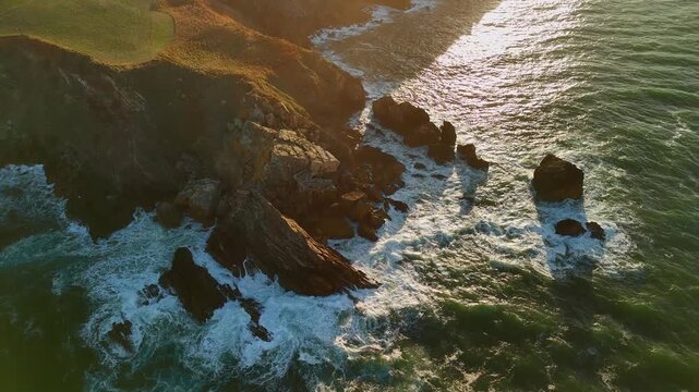 Aerial drone gliding left to right in half circle above rocky coastline with crashing ocean waves in Spain