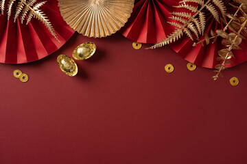 Fototapeta premium Vibrant red backdrop with gold coins, paper fans, and dried foliage captures the festive mood of Chinese New Year greetings and celebration with a luxurious, auspicious feel