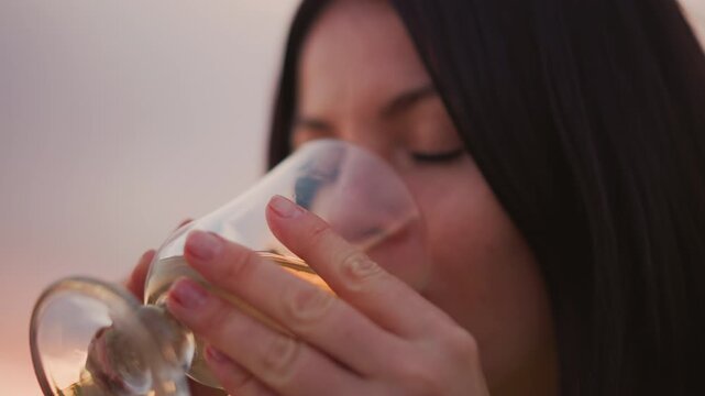 woman sips drink at sunset in open meadow, closeup on glass and hands then contemplative portrait, warm amber glow on face, stemware held gently, relaxed evening mood and soft horizon backdrop