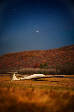 Glider plane parked on the grass and covered at night airport under night starry sky